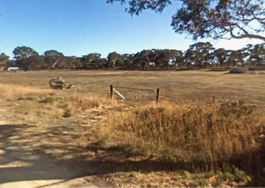 Rural property entrance before works, with a farm gate and long grass beside the road